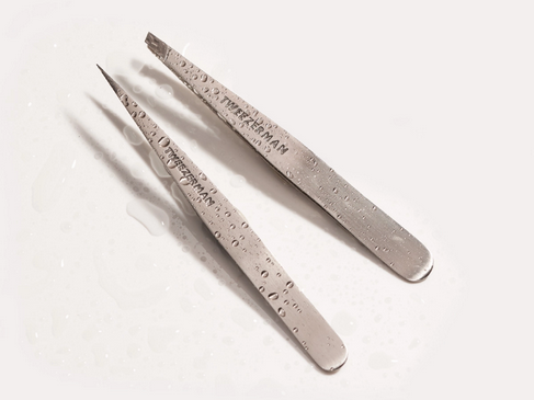 Stainless Steel Tweezerman tweezers, on a counter with water drops.