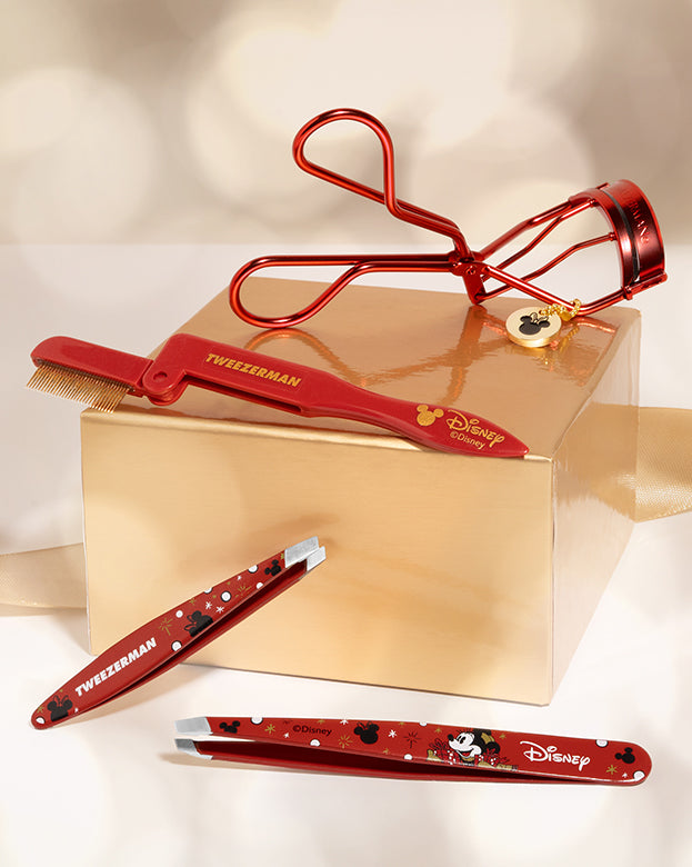 Disney Mickey Mouse and Minnie Mouse Magic All Around Collection featuring a red eyelash curler and lash comb, a red mini slant tweezer and full slant tweezer with Minnie mouse illustration, and black mickey ears.