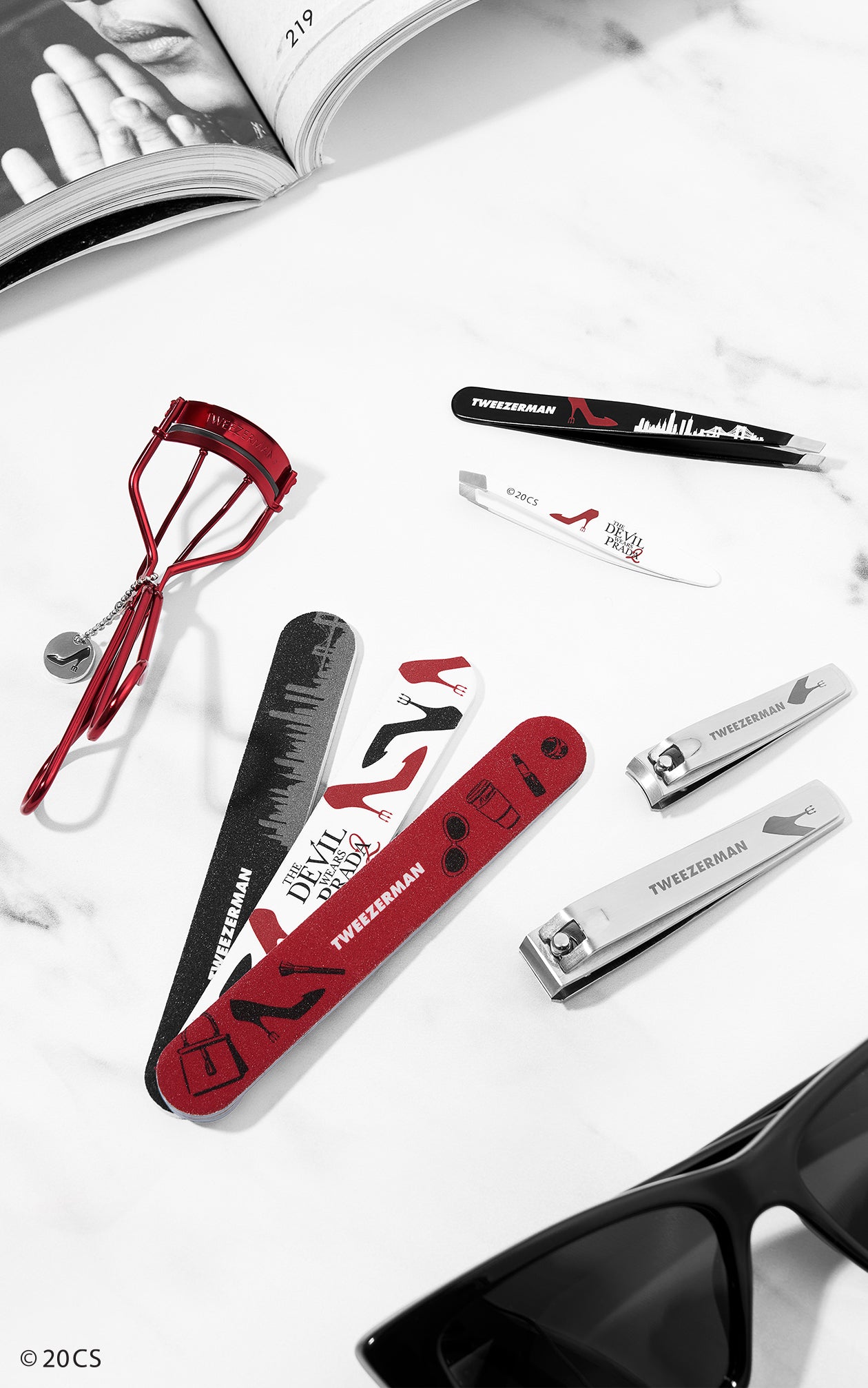 Set of beauty tools from Tweezerman's The Devil Wears Prada 2 Collection including The Devil Wears Prada 2 Slant Tweezer in black and white,
The Devil Wears Prada 2 Mini Slant Tweezer in white,
The Devil Wears Prada 2 Curler in red,
The Devil Wears Prada 2 Combo Clipper Set in stainless steel,
The Devil Wears Prada 2 Nail File Set of 3 in red, black and white,
 on a white background