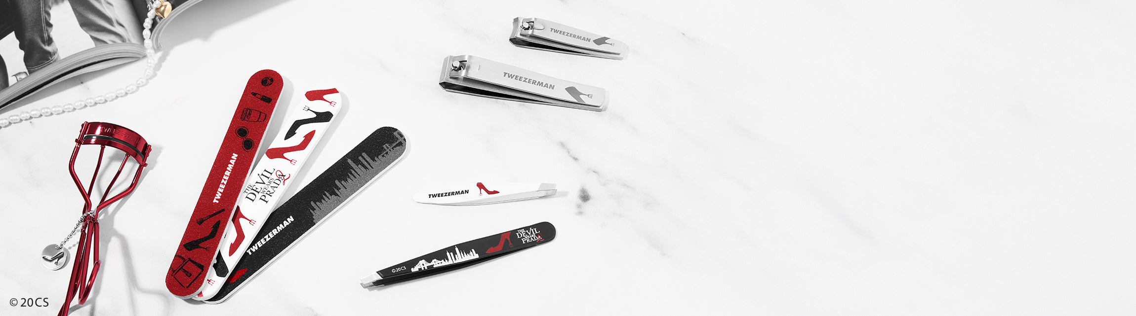 Set of beauty tools from Tweezerman's The Devil Wears Prada 2 Collection including The Devil Wears Prada 2 Slant Tweezer in black and white,
The Devil Wears Prada 2 Mini Slant Tweezer in white,
The Devil Wears Prada 2 Curler in red,
The Devil Wears Prada 2 Combo Clipper Set in stainless steel,
The Devil Wears Prada 2 Nail File Set of 3 in red, black and white,
 on a white background