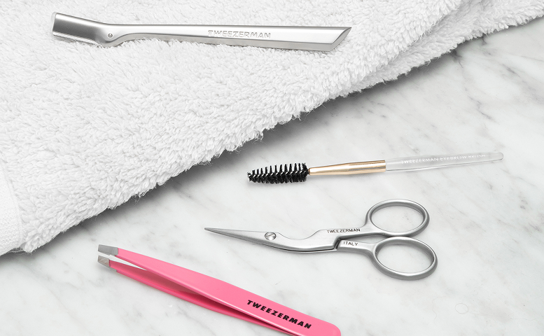 Tweezerman Beauty tools on a grey and white marble top with white towel.