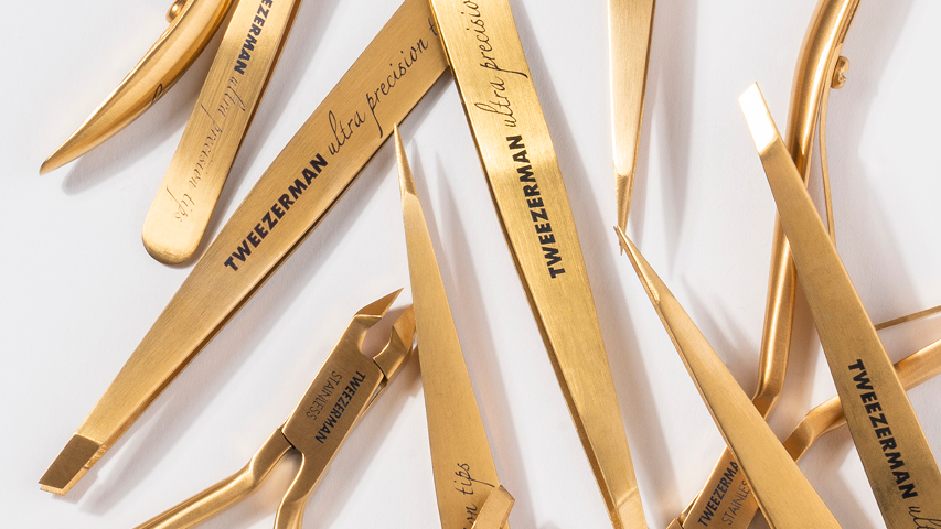 Gold Tweezerman Ultra Precision beauty tool collection laid out on a white surface.