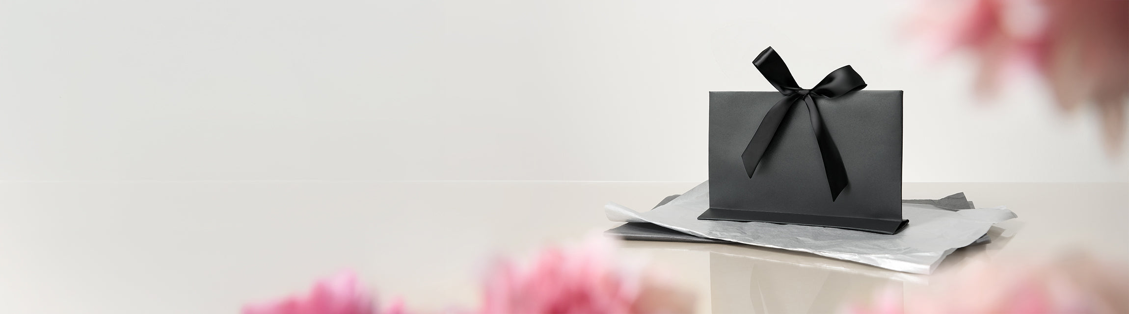 Black gift box with a bow on a light surface with blurred floral background