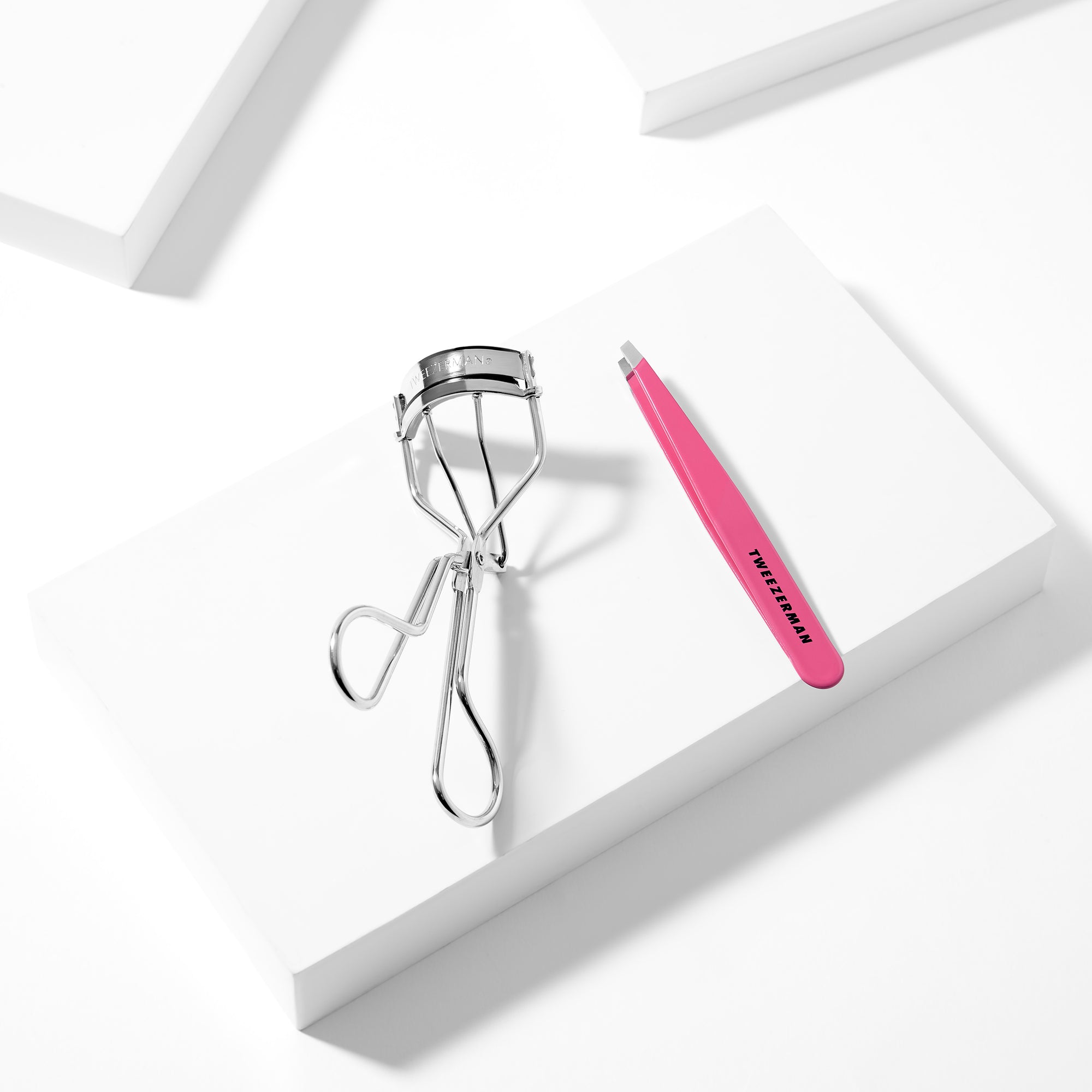 Eyelash Curler and Pink Slant Tweezer placed on a white block tray