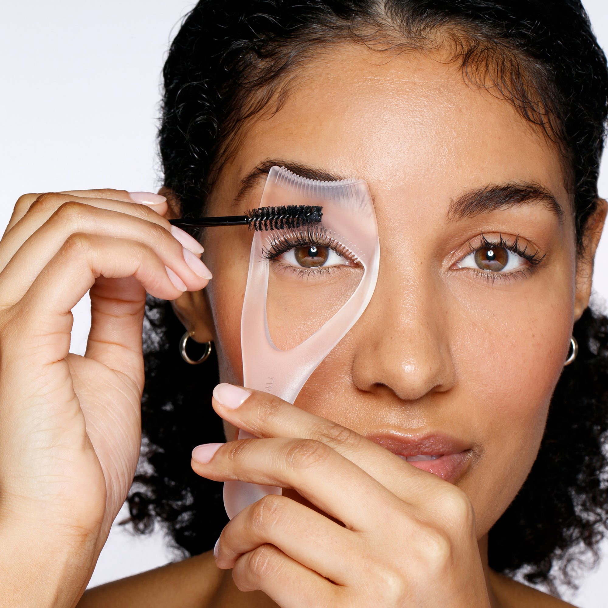 Model using lash guard and comb to apply mascara on top lashes