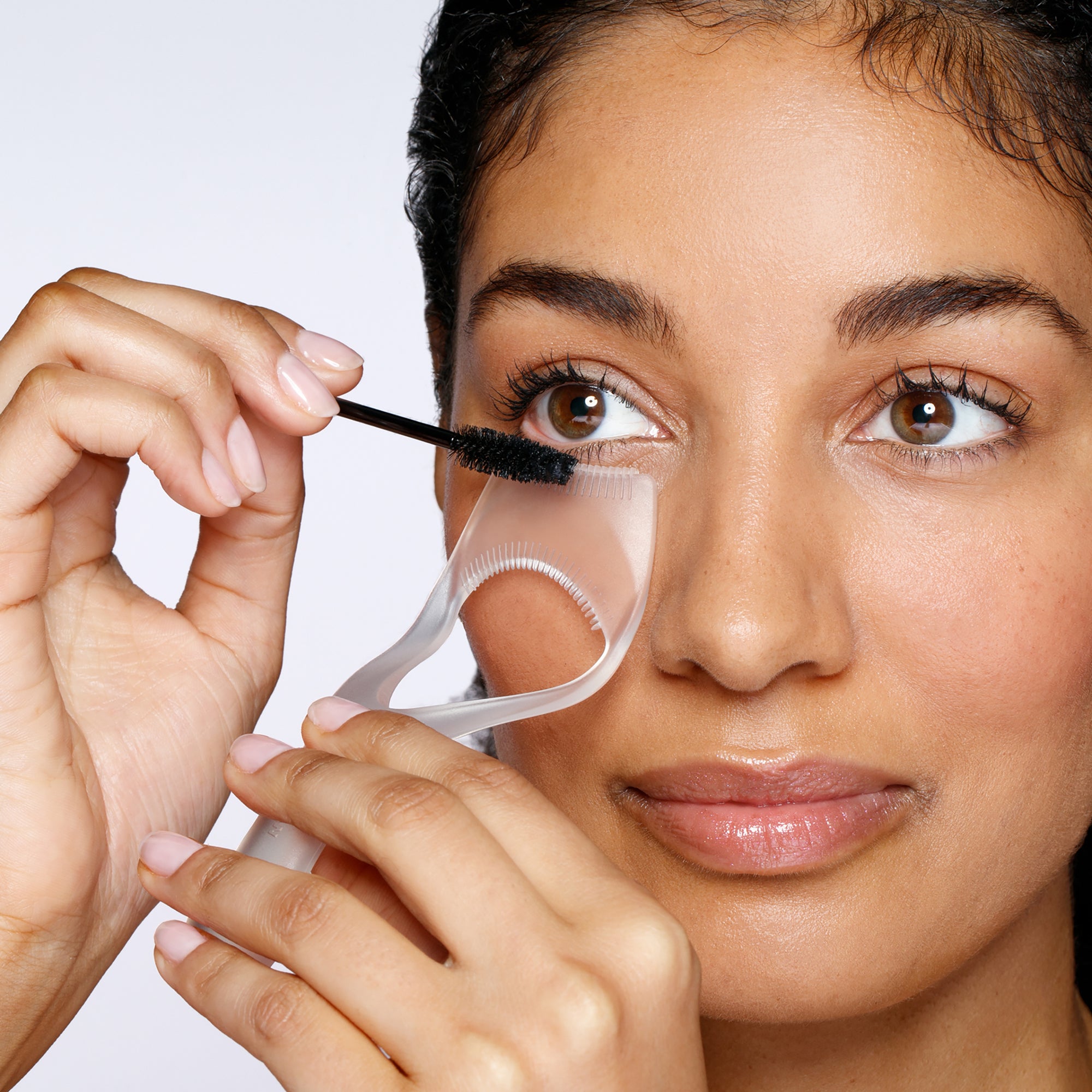 Model using lash guard and comb to apply mascara on bottom lashes